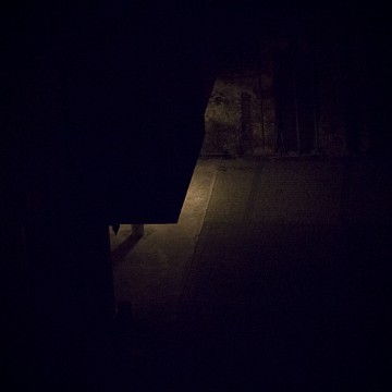 Plano general cenital, color. Portal de calle oscura iluminado por solo una luz escondida.