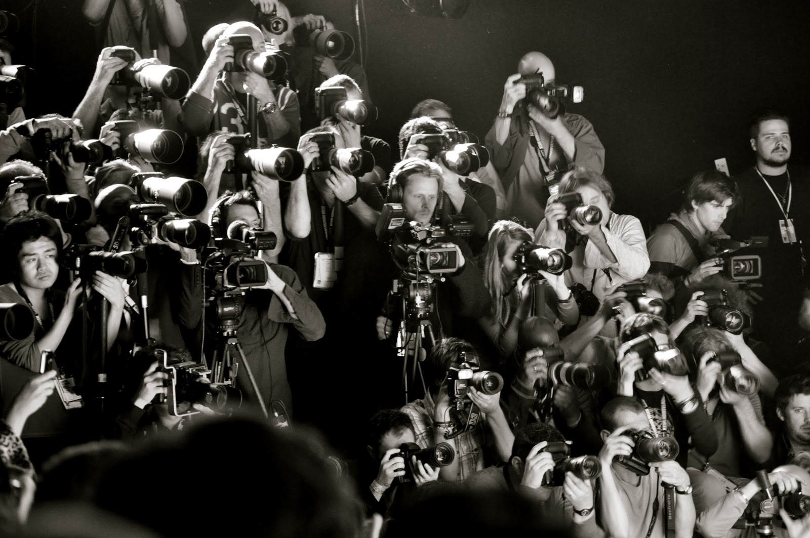 Plano general, blanco y negro. Multitud de fotógrafos al final de una pasarela de una semana de la moda disparando sus cámaras