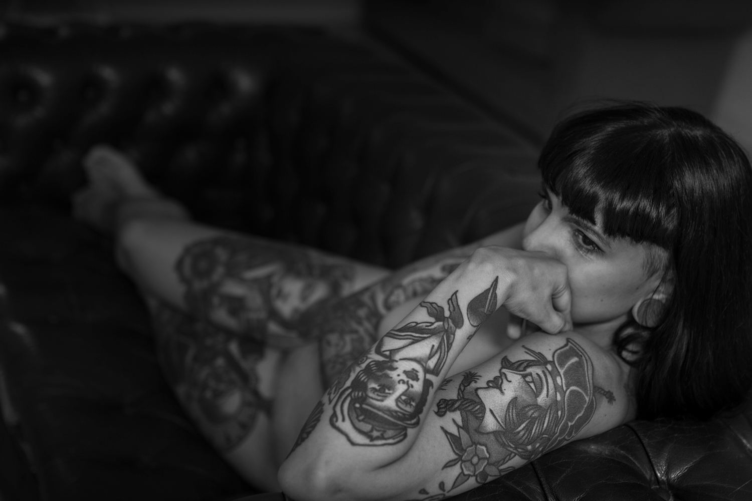 Blanco y negro, plano general. Modelo, tatuada y desnuda, recostada en un sofá en actitud pensativa.