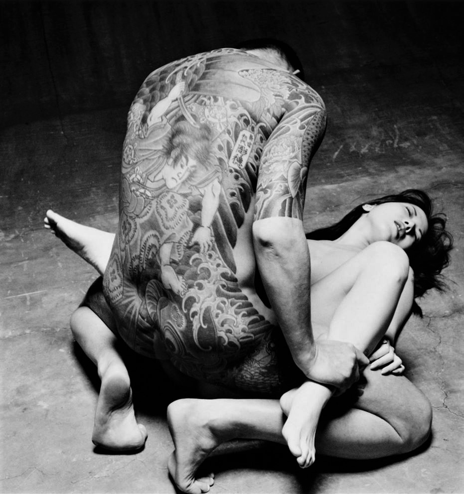 Pornografía y arte. Yakuza tatuado, de espaldas, manteniendo relaciones sexuales, de rodillas, con una mujer, oriental, acostada en el suelo.
